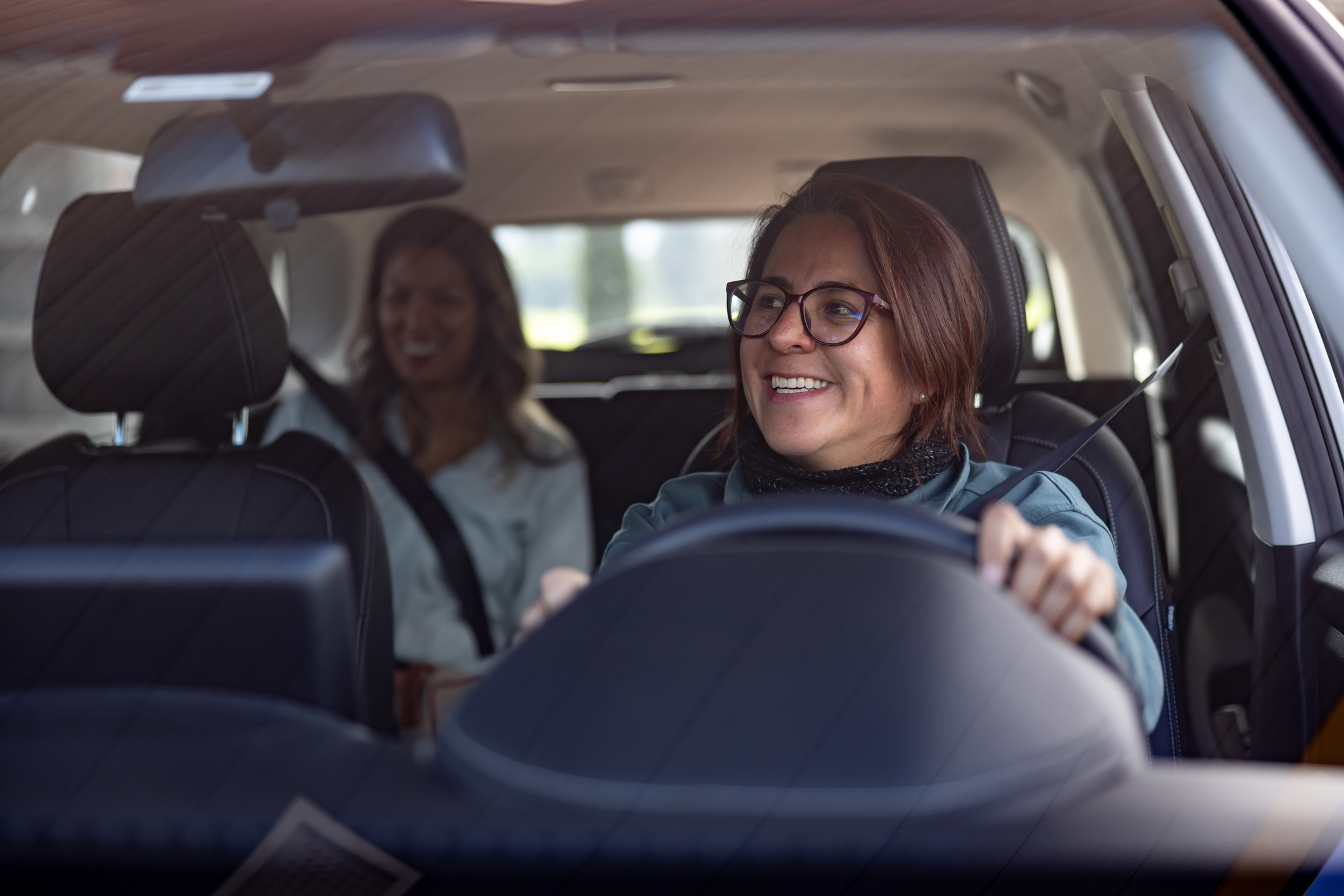 Happy female taxi driver talking to a passenger in the back seat and looking through the rear view mirror