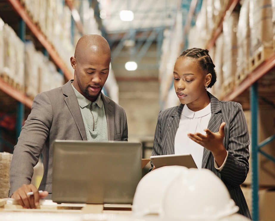 Collaboration, planning and people with laptop, factory or quality control for distribution with tech. Warehouse, teamwork and engineer with checklist for goods, logistics and discussion for shipping A man and a woman looking at a computer