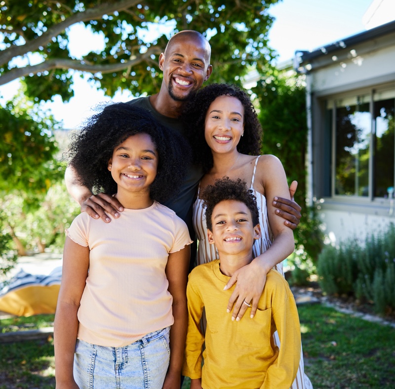 Smiling parents standing with their two children outside in their yard